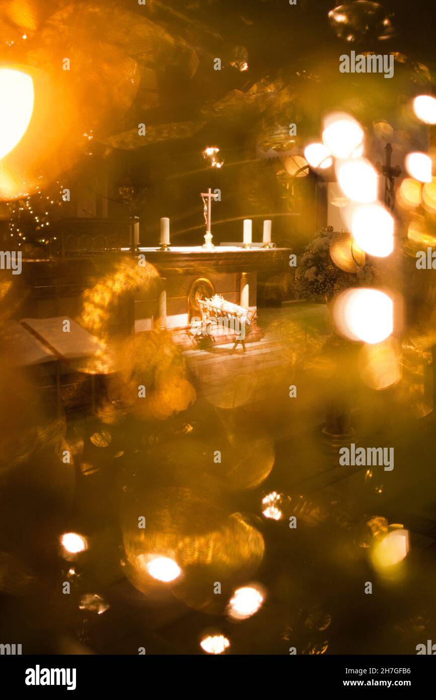 Baby Jesus in the manger, Christmas light on the trees in the background, artistic photography, photos over the christmas tree looking into the church Stock Photo