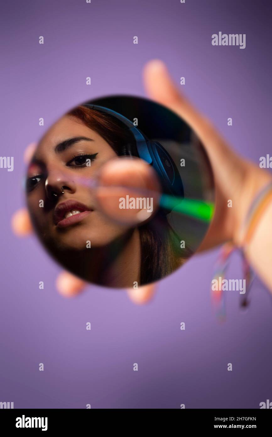 A girl is reflected on a cd held in her hand while listening to music whit headphones Stock Photo