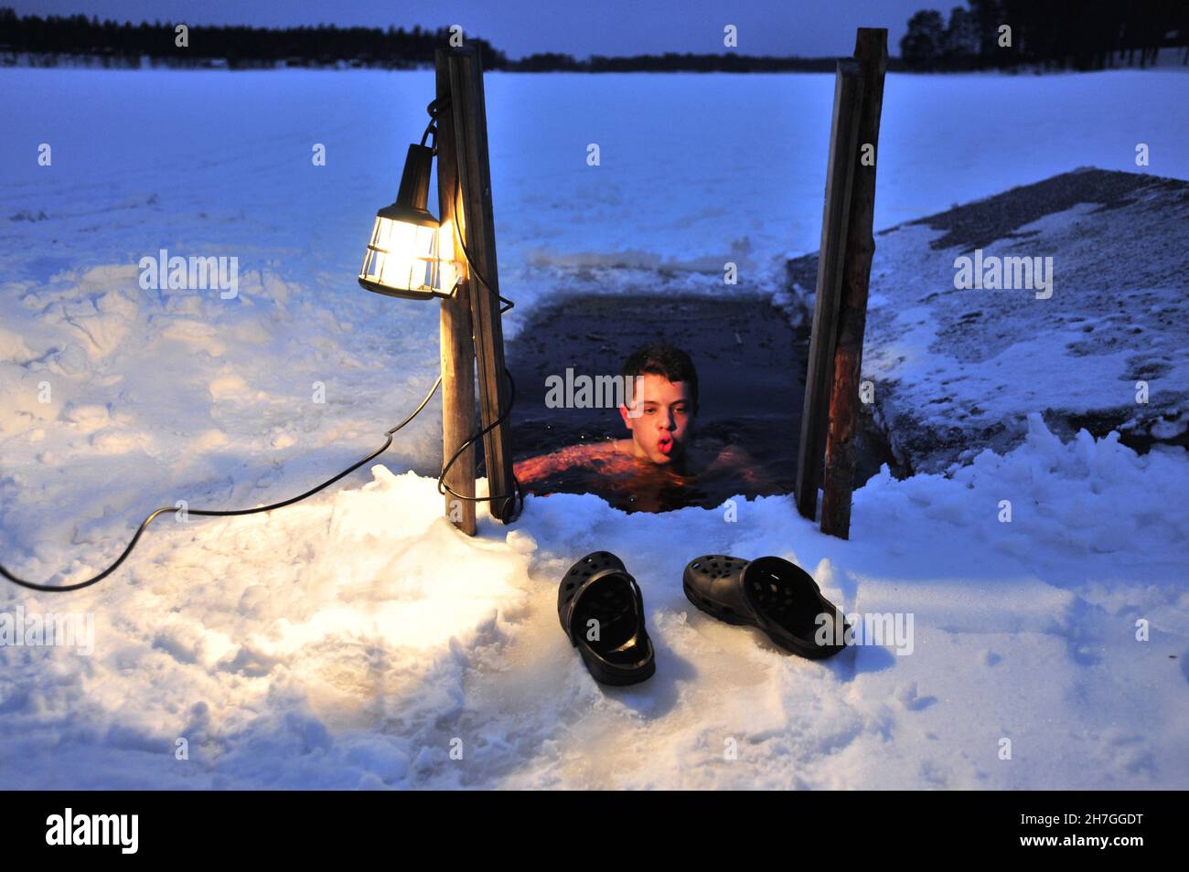 SCANDINAVIA. FINLAND IN WINTER. HOSSA NATIONAL PARK. MAN HAVING A BATH IN AN ICED LAKE AFTER A SAUNA. Stock Photo