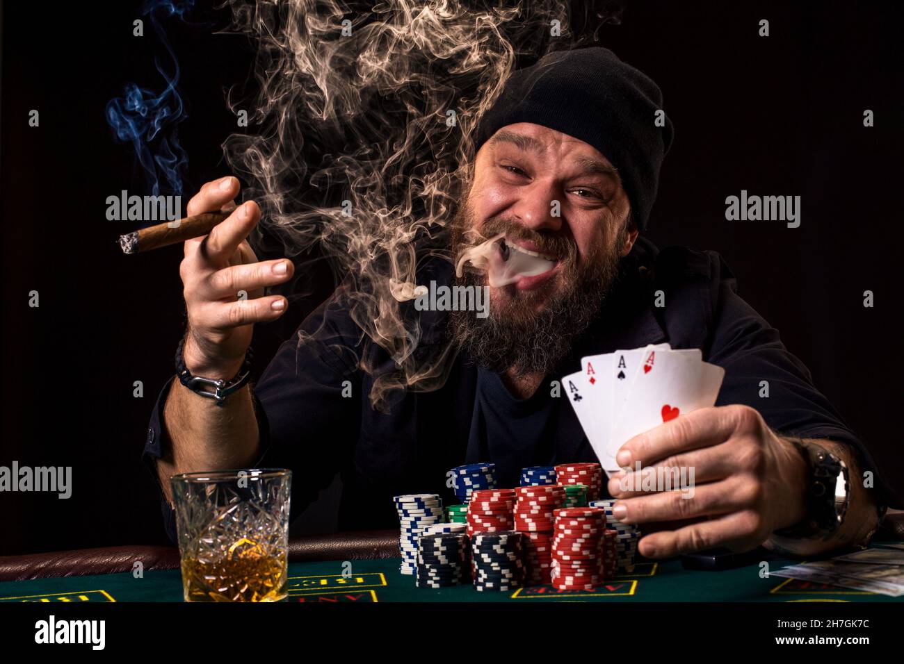 Bearded man drinking whisky and smoking a cigar while playing poker