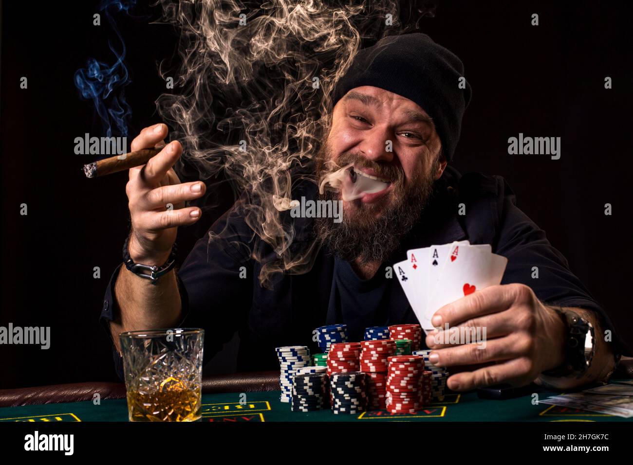 Bearded man drinking whisky and smoking a cigar while playing poker Stock Photo