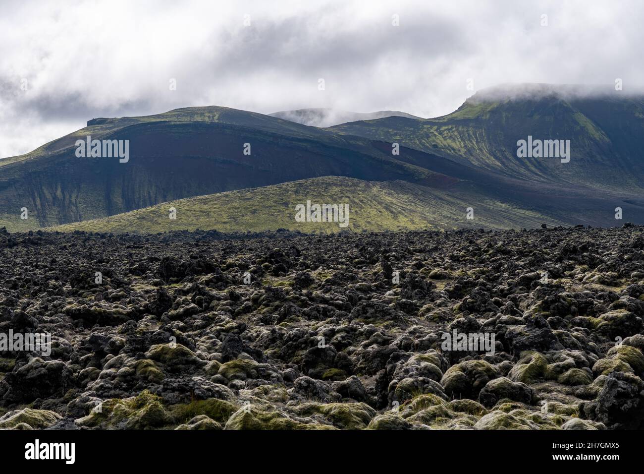 Low angle view of the barren landscape of black lava rock from the nearby Katla volcano on Iceland with mountains in the background Stock Photo