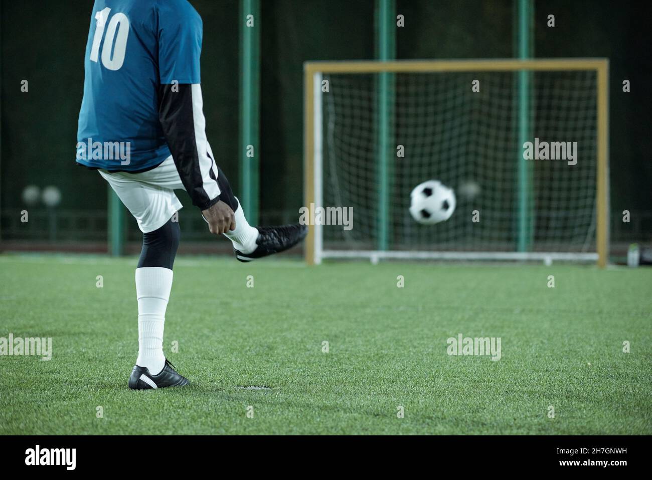 Back view of low section of footballer kicking soccer ball in direction