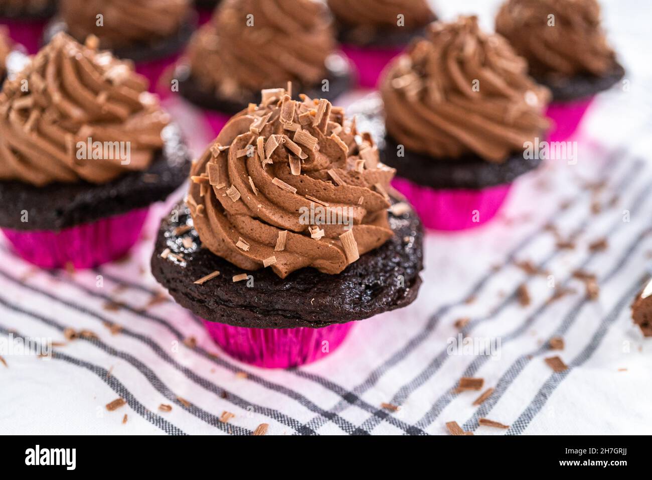 Piping chocolate ganache frosting on top of chocolate cupcakes Stock