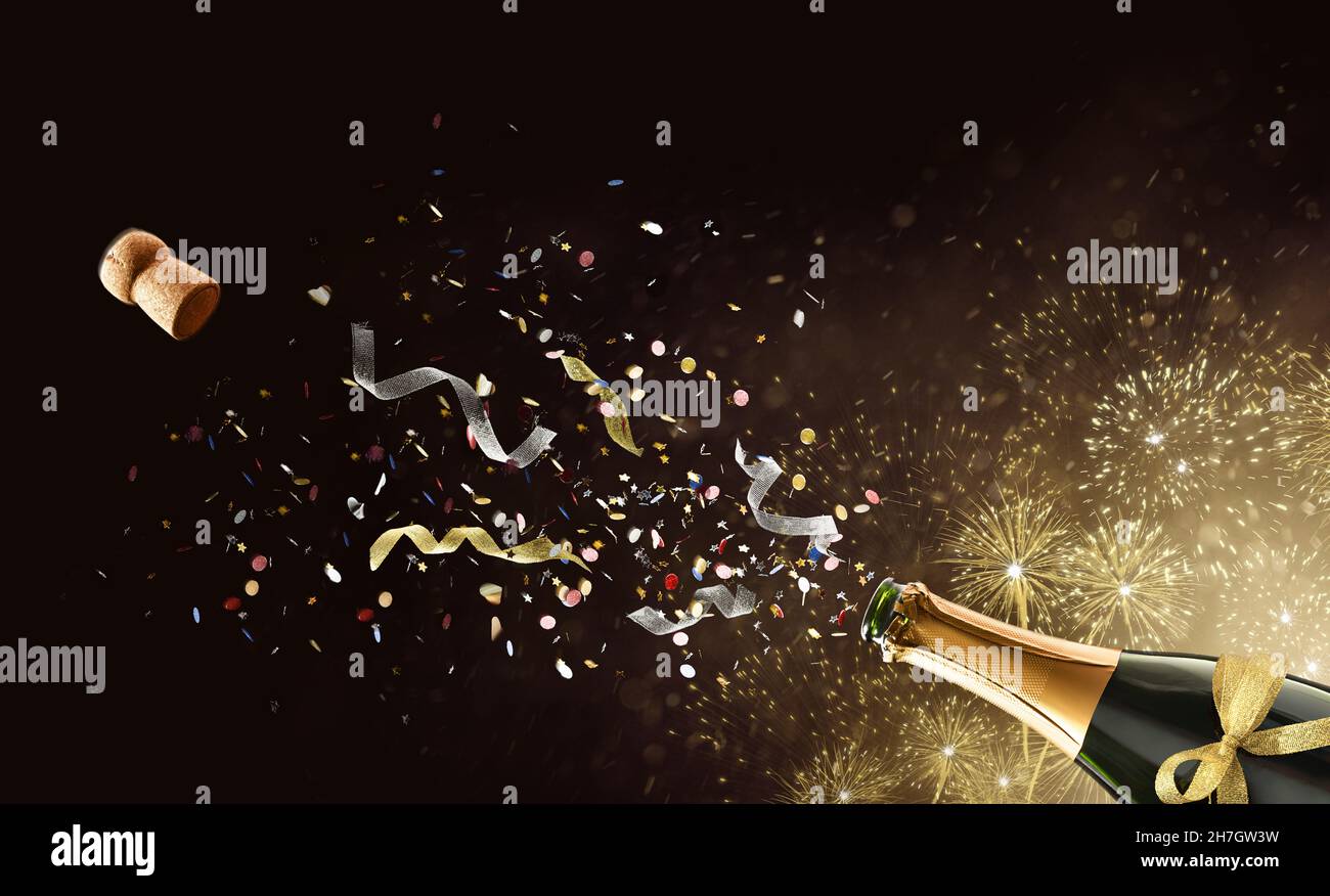 Festive concept with freshly opened bottle of sparkling wine with confetti and ribbons coming out on golden isolated background with fireworks Stock Photo