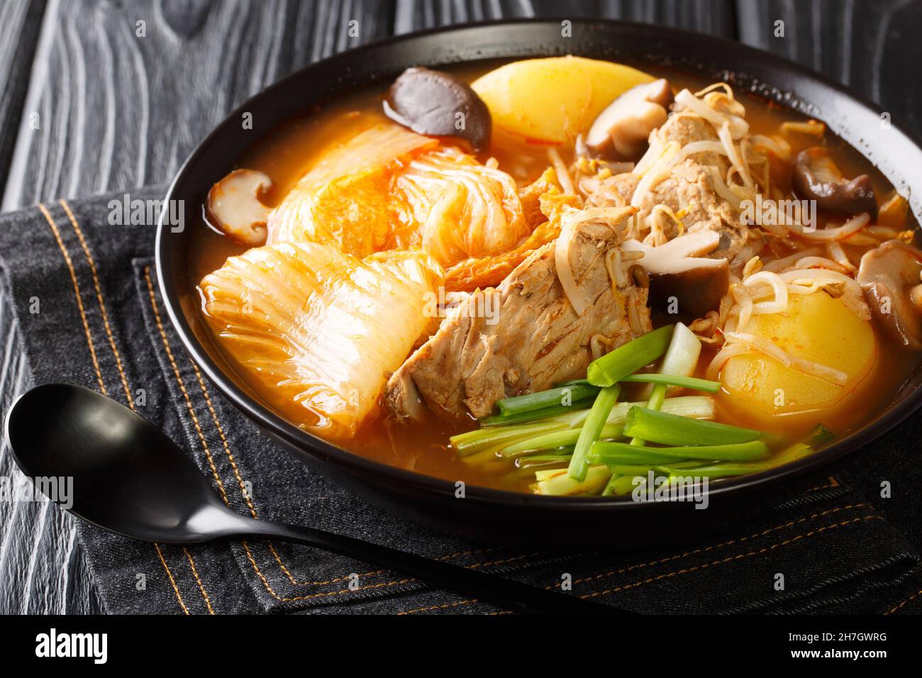 Korean Gamjatang is a spicy hearty stew made with pork bones close up in the bowl on the table. Horizontal Stock Photo