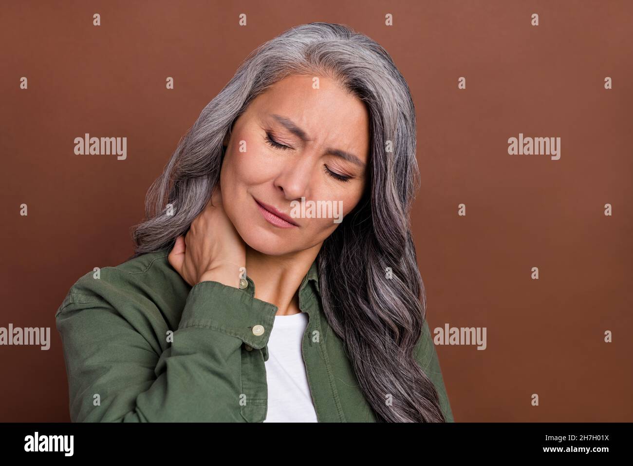 Photo of sad elder white hairdo lady hand neck wear shirt isolated on brown color background Stock Photo