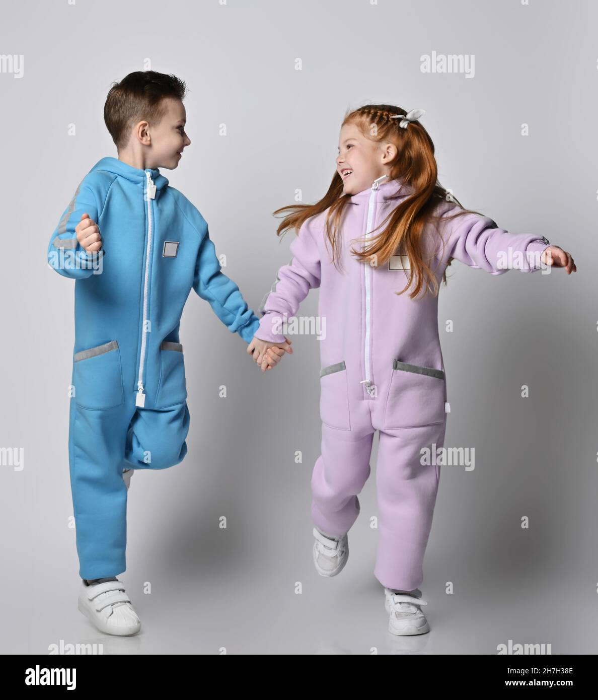 Playful frolic kids boy and girl in blue and pink jumpsuits with are running together looking at each other Stock Photo