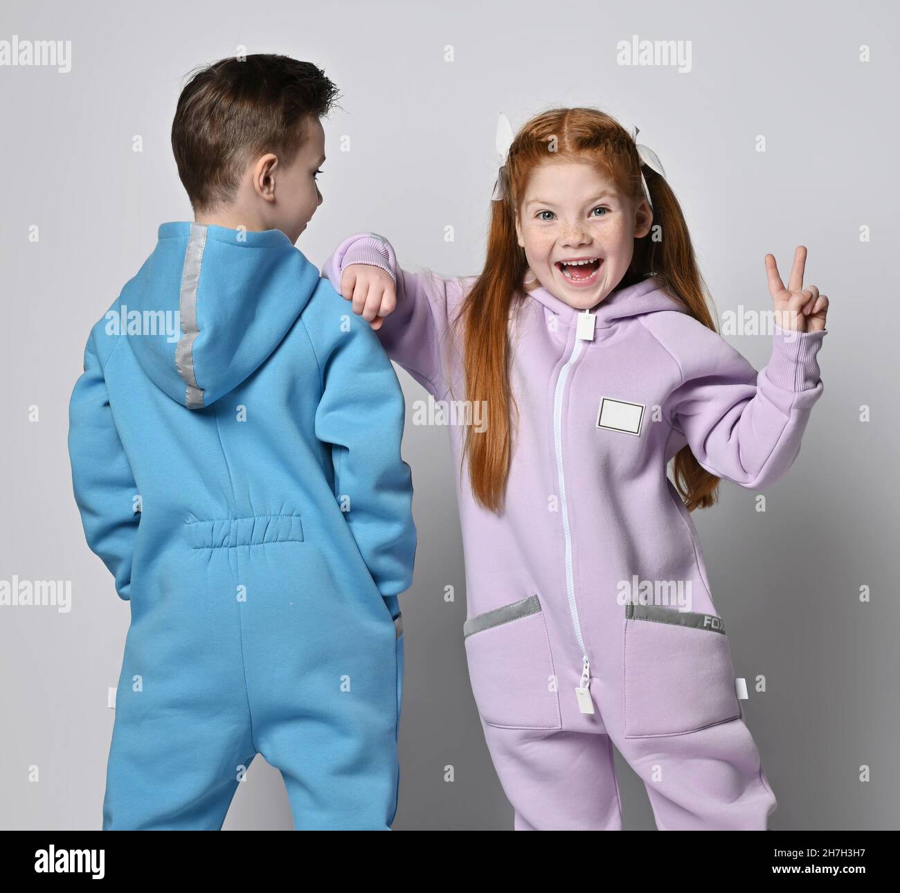 Frolic kids in blue and pink jumpsuits are standing next to each other, boy with his back to us and girl with her face Stock Photo