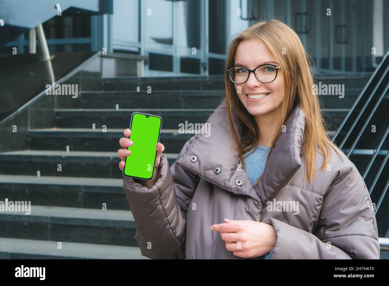 Beautiful smiling caucasian girl with glasses showing blank smart phone green screen Stock Photo