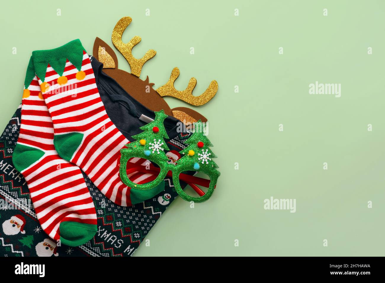 Merry Christmas. Top view of christmas sweater with christmas socks,bright Christmas toy deer antlers and funny glasses over green background. Christm Stock Photo