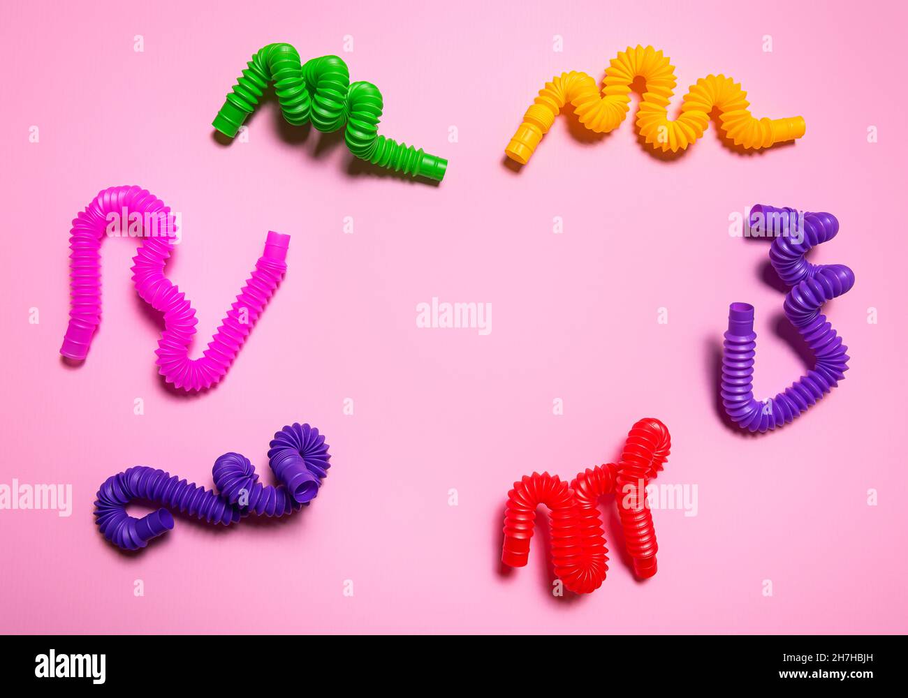 Colorful red, purple, pink, green and yellow pop tube children toys bent in different shapes. Cheerful plastic antistress multicolored toy set on pink Stock Photo