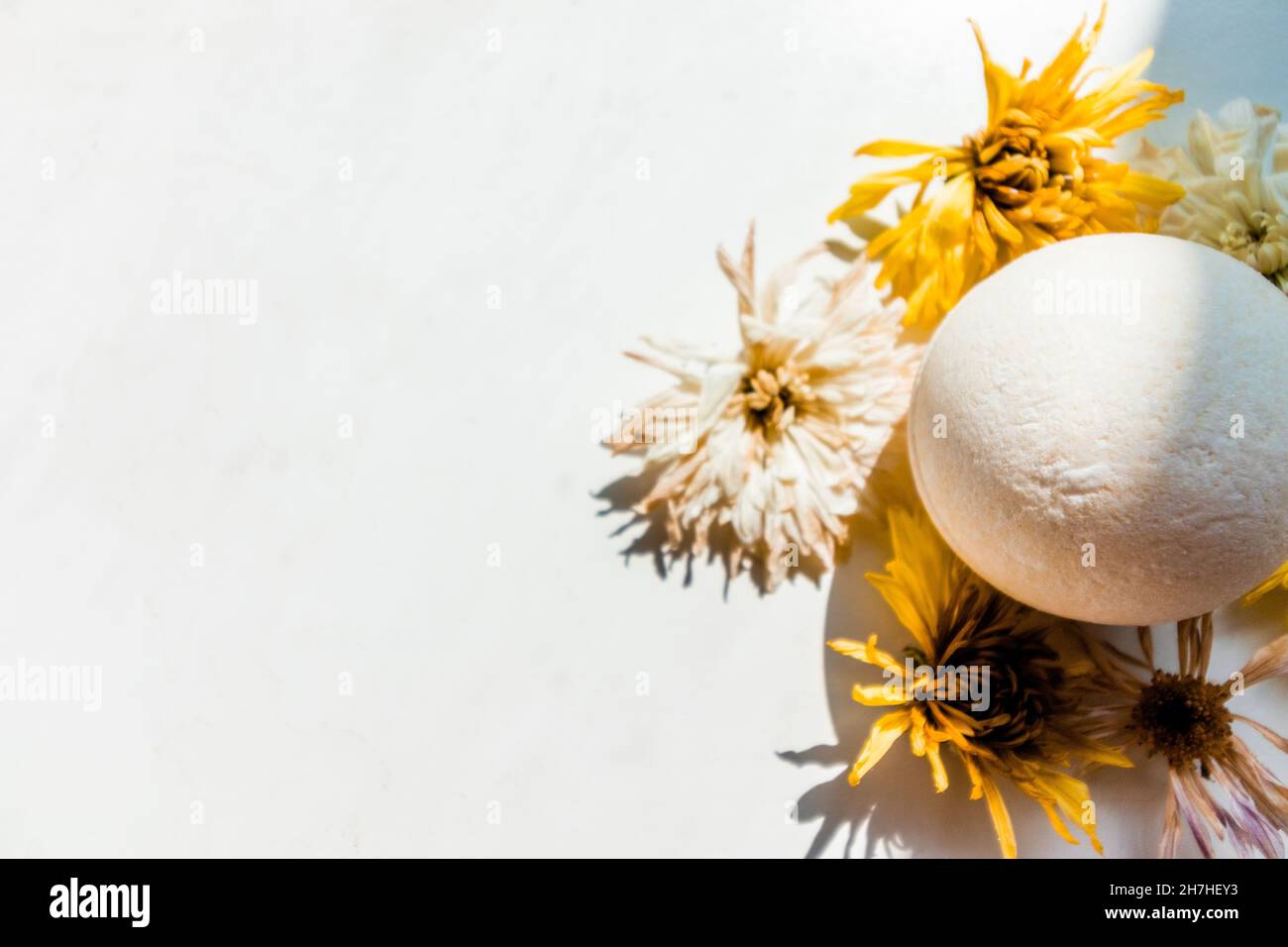 White bath bomb among dried flowers on a white background.  Stock Photo