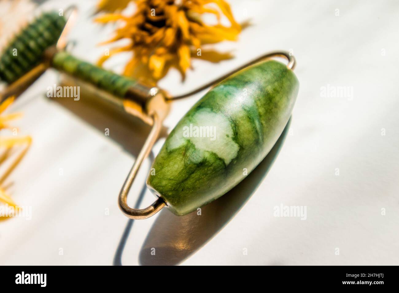 Green jade roller facial massager close-up on a background of dry buds.  Stock Photo