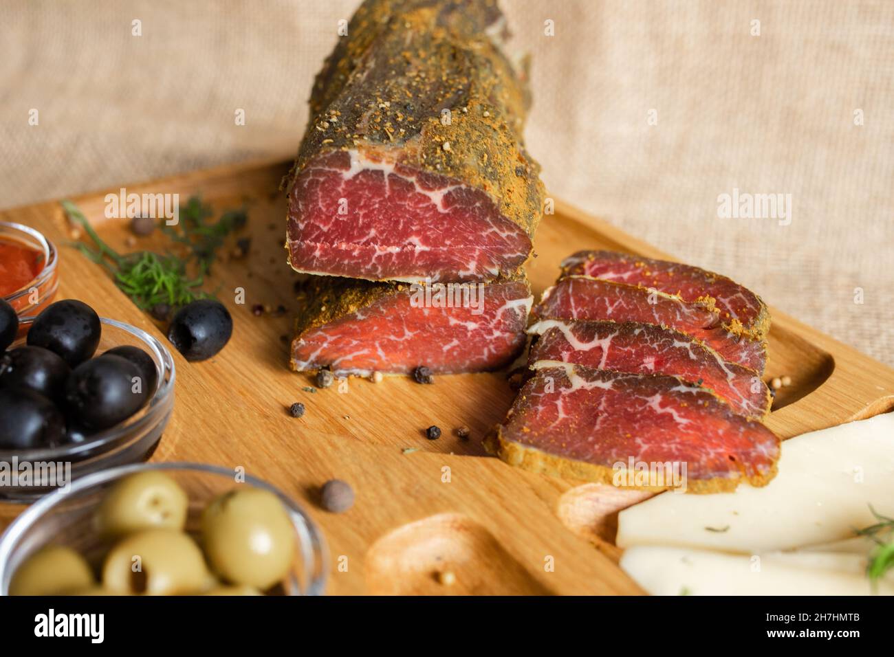 Dried tenderloin of beef meat, thinly sliced, on the wooden serving board with cheese, olives, black pepper, tomato sauce. Jerky tenderloin appetizer Stock Photo