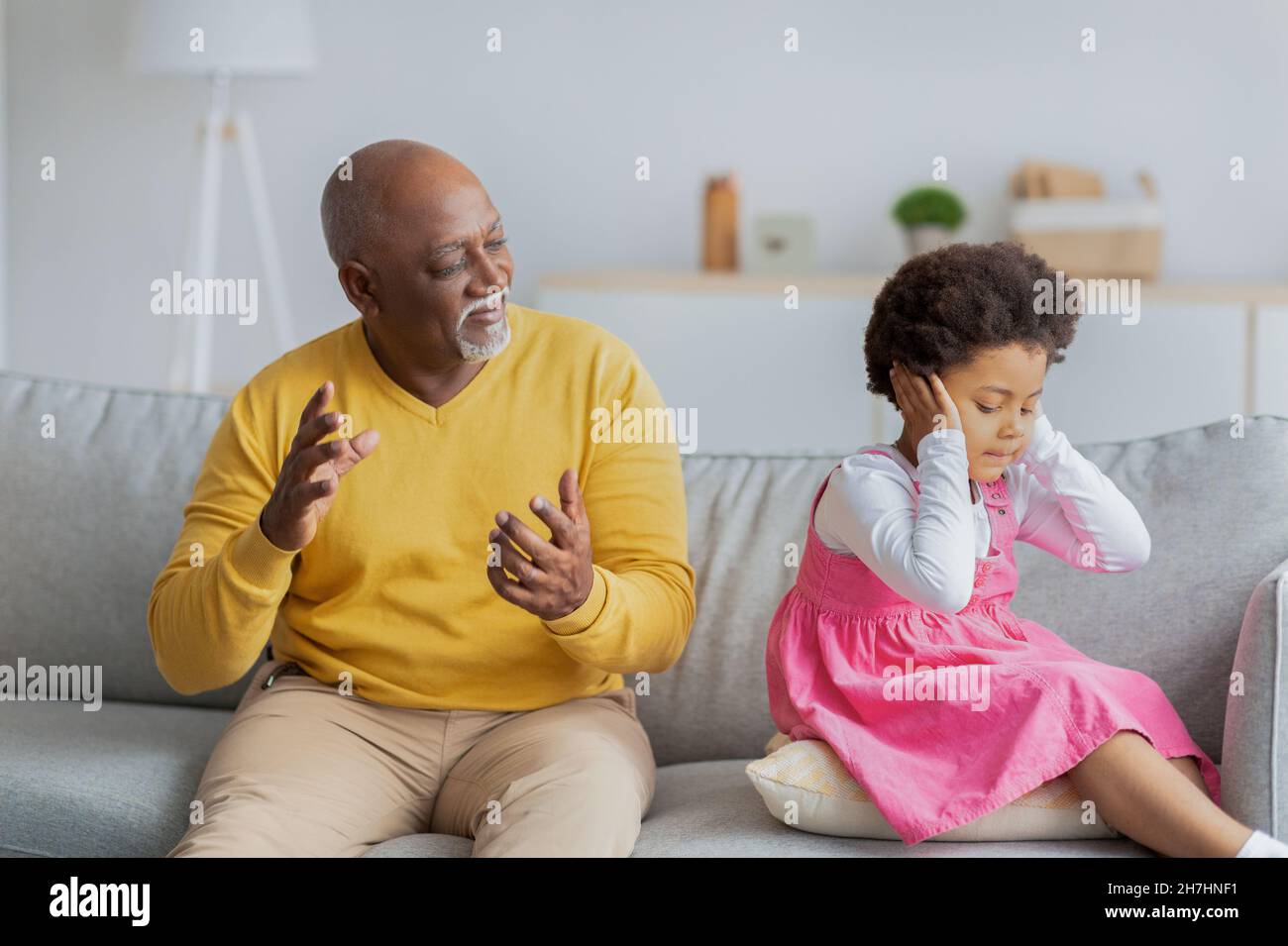 Upset sad black little girl closes her ears and does not want to listen to elderly man Stock Photo