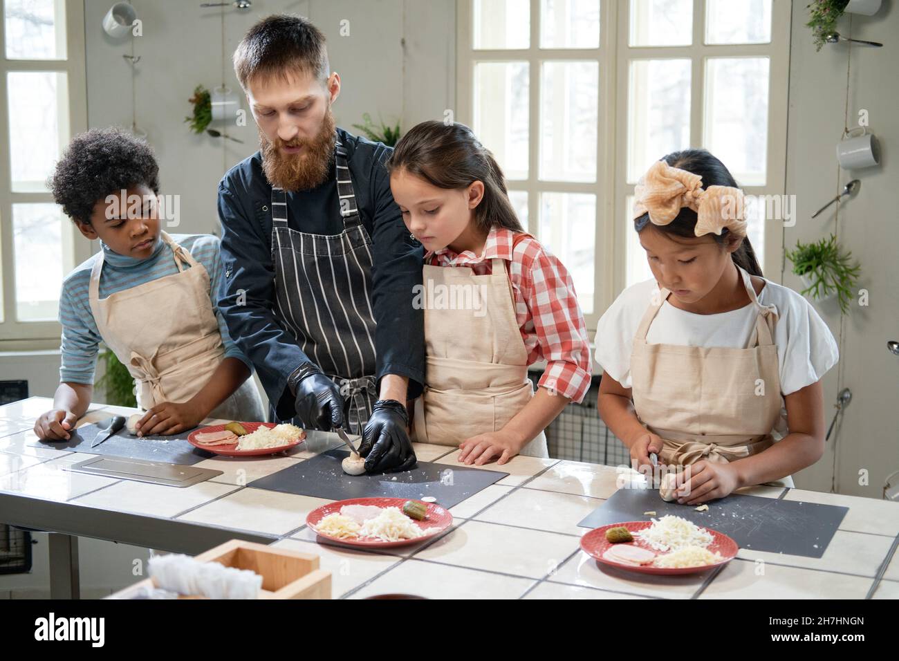 Young cook in apron teaching children to cut the mushrooms for pizza