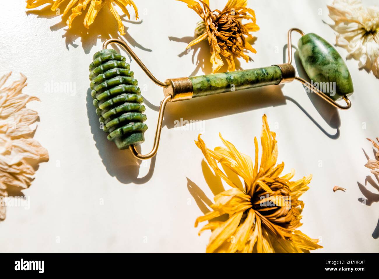 Jade massager roller for the face on a white background next to buds of flowers. Stock Photo