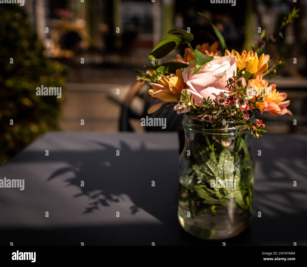 A glass vase with colourful flowers on the table in the restaurant. Sunny day, no people. Background with copyspace. Stock Photo