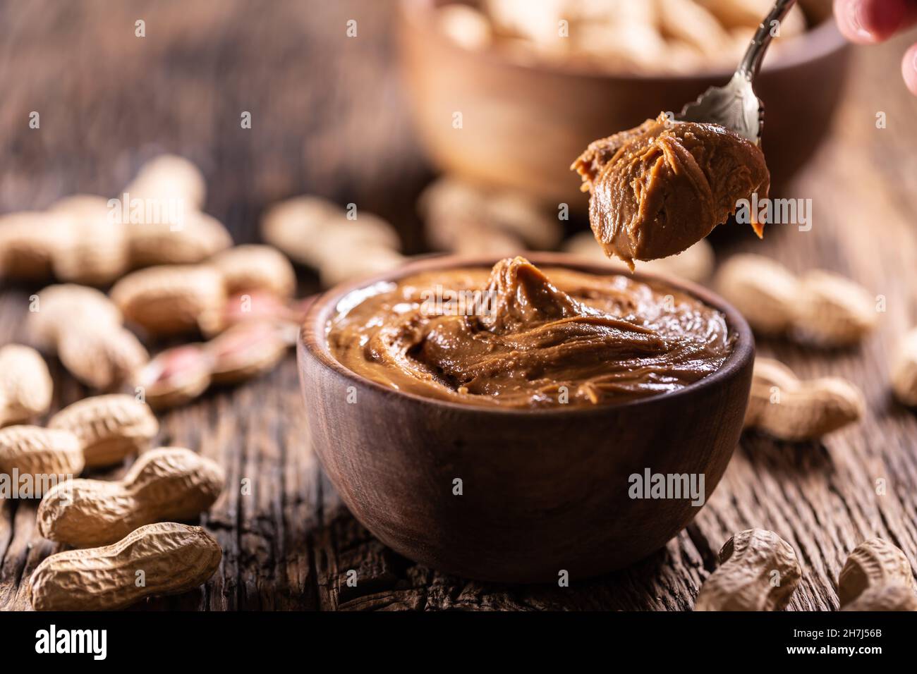 Peanut butter on spoon bowl and peanuts on wooden table. Stock Photo