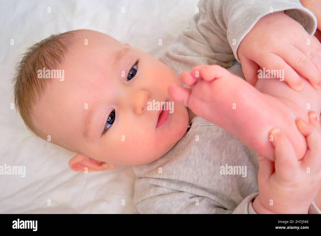 Happy infant baby boy pulls his leg into his mouth and smiles. Four