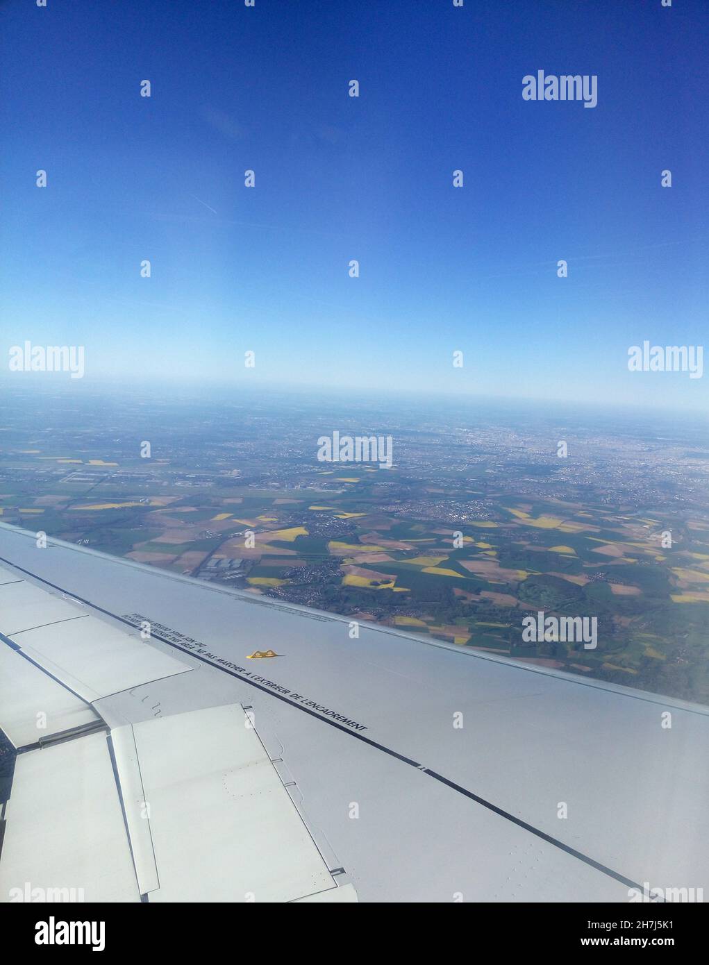 Airplane wing and land far under the plane. Flight in the deep blue sky Stock Photo