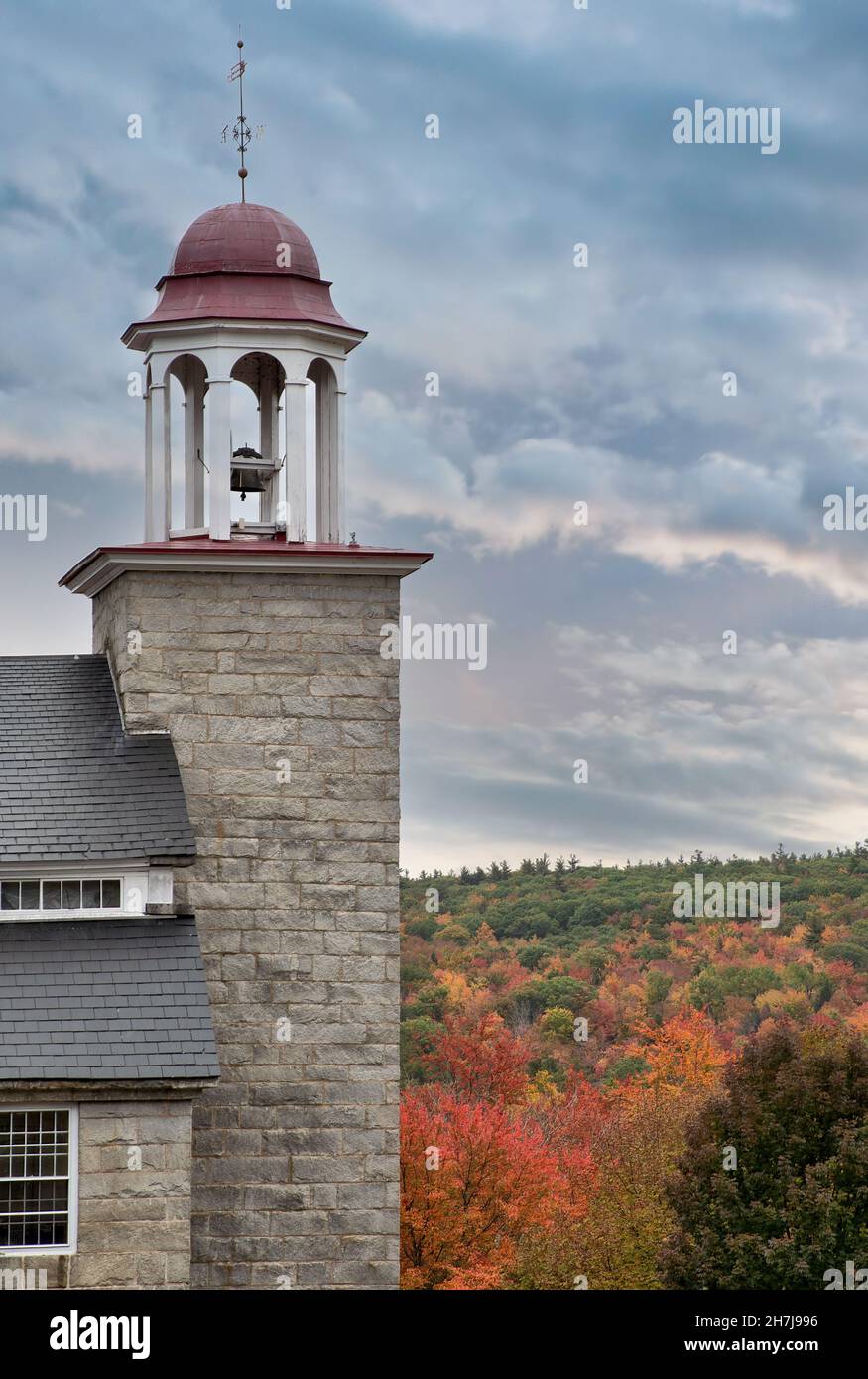 Colorful autumn sky, brilliant fall foliage, and granite bell tower of preserved textile mill building constructed in 1846 in Harrisville village. Stock Photo