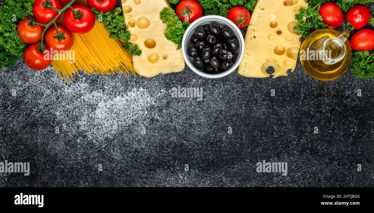 Food cooking background with copy space. Recipe Ingredients. Cherry tomatoes, oil, olives, spaghetti, Dutch cheese and parsley on a dark board. Templa Stock Photo