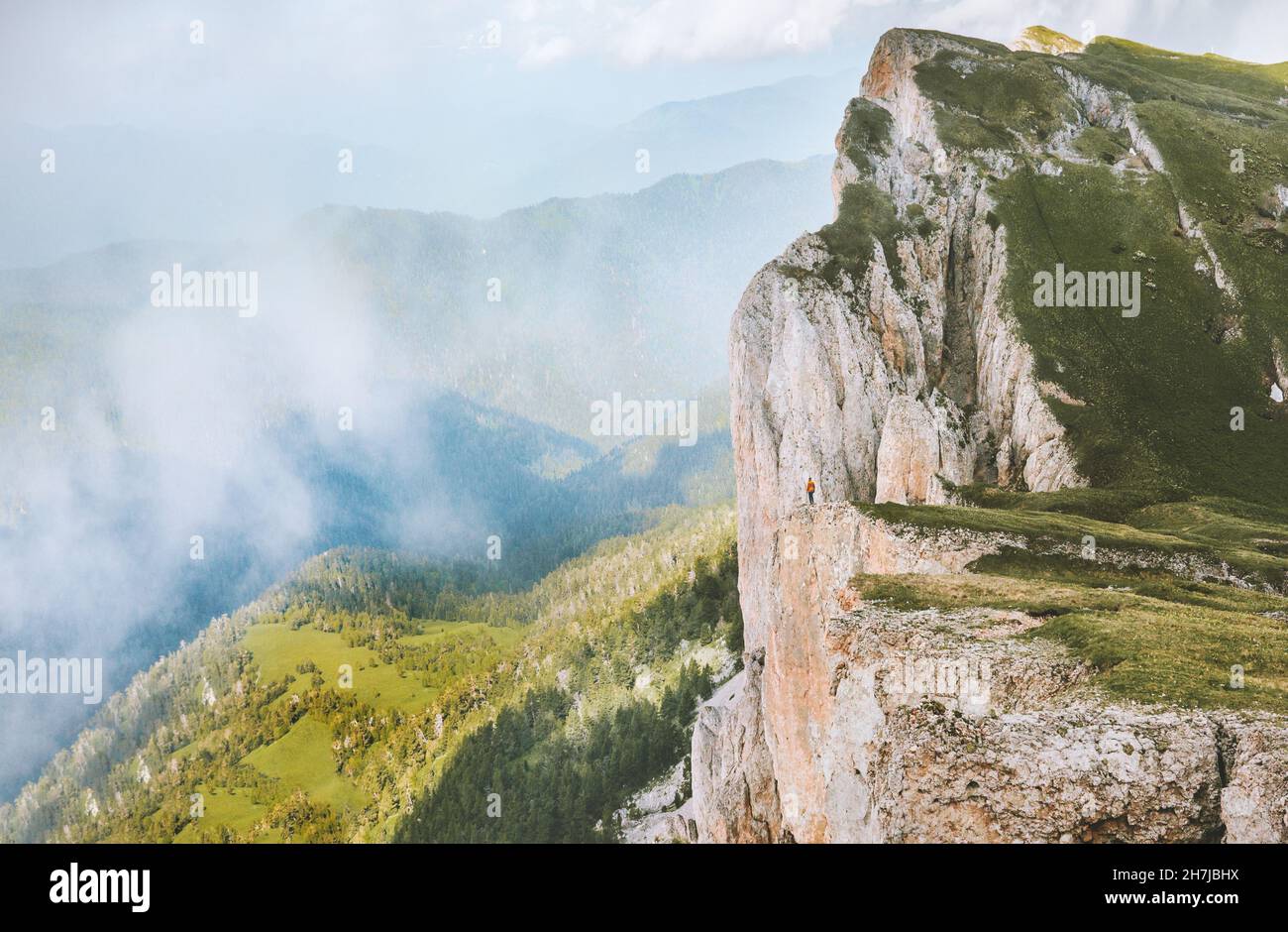 Mountain climbing travel adventure vacations outdoor man standing on cliff edge rocks and clouds landscape Stock Photo