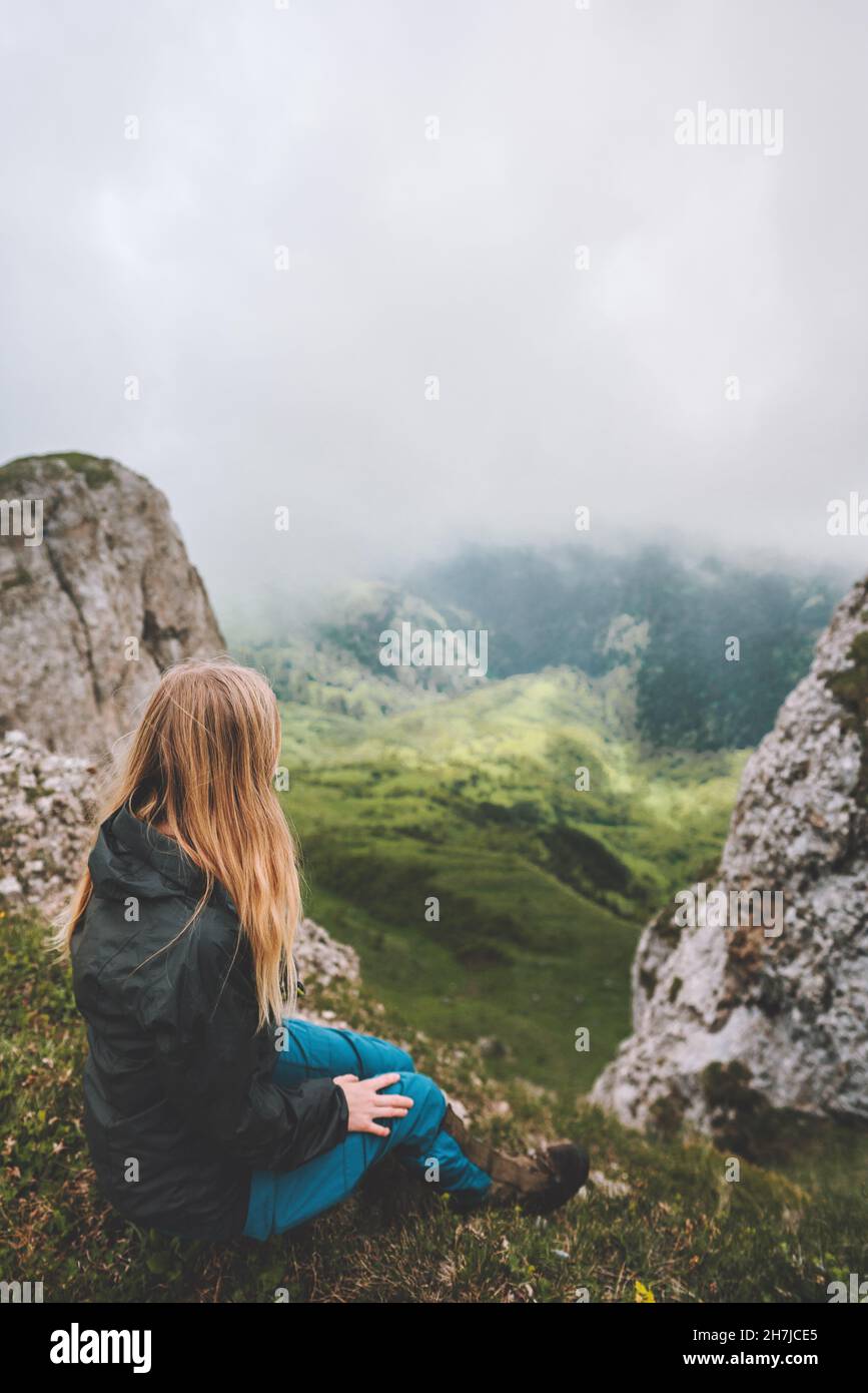 Woman sitting on cliff edge alone looking at aerial foggy view hiking solo outdoor healthy lifestyle summer vacations Stock Photo