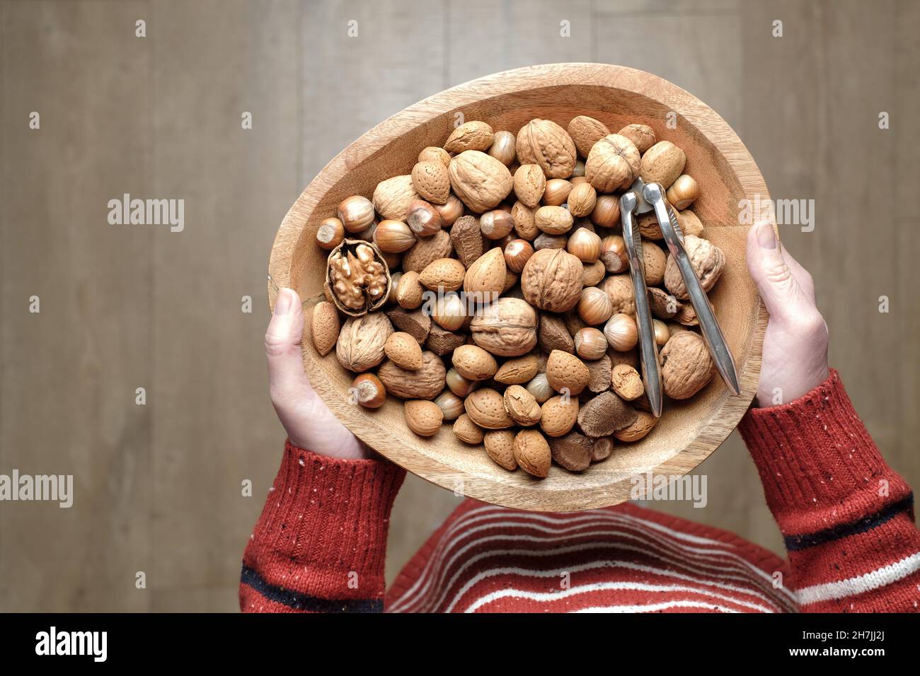 A woman holding a wooden bowl of mixed traditional Christmas nuts, still in their shells, along with a traditional metal nut cracker Stock Photo