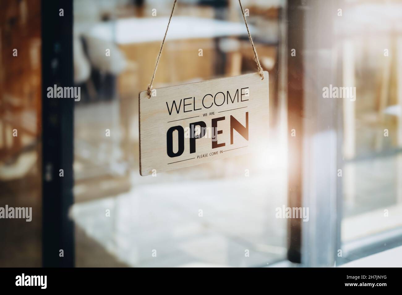 WELCOME WE ARE OPEN PLEASE COME IN notice sign wood board label hanging through glass door. Stock Photo