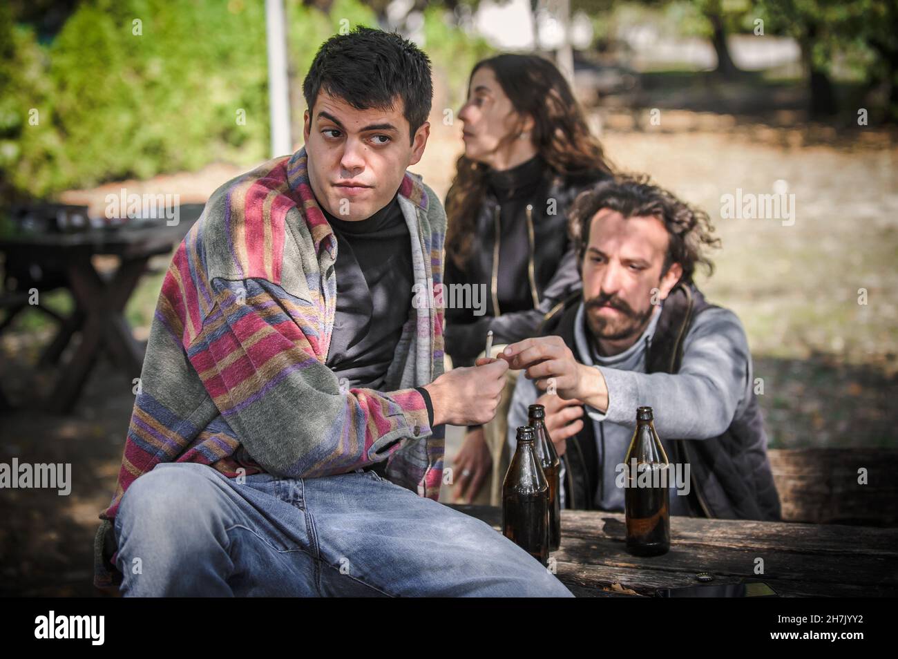 Young friends keep watch, look around and try to hide while gives from hand to hand each other ganja joint in public park outdoor. Smoking cannabis ma Stock Photo