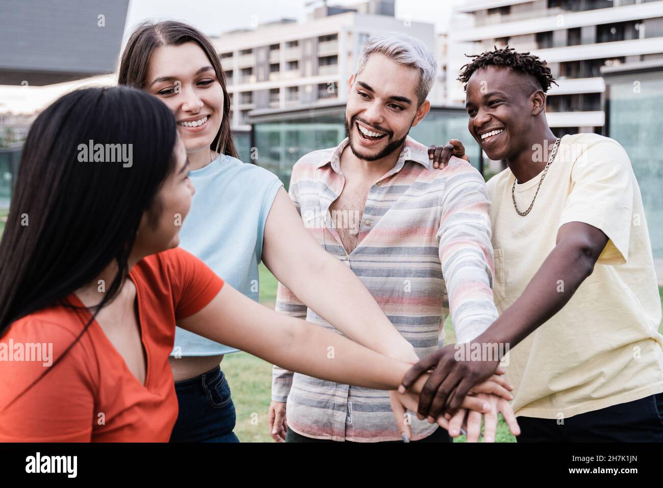 Young diverse group of people celebrating together stacking hands outdoor - Focus on gay man wearing makeup Stock Photo