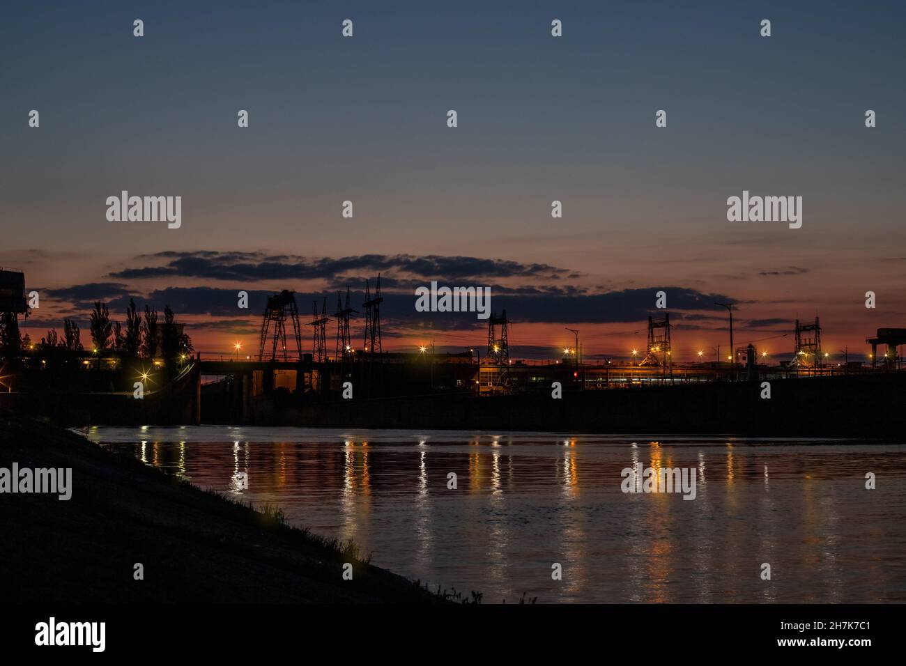 Dam at night. Concrete dam on the river. Night city with lights at beautiful sunset Long exposure view dam and city on sunset, vivid, blurry Stock Photo