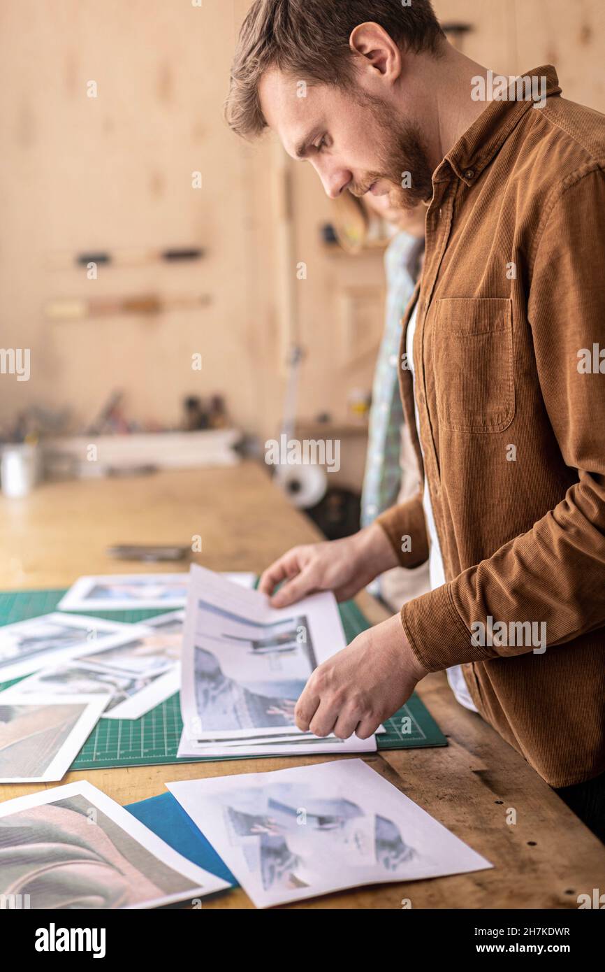 Male professional tanner looking pictures paper photos work examples of