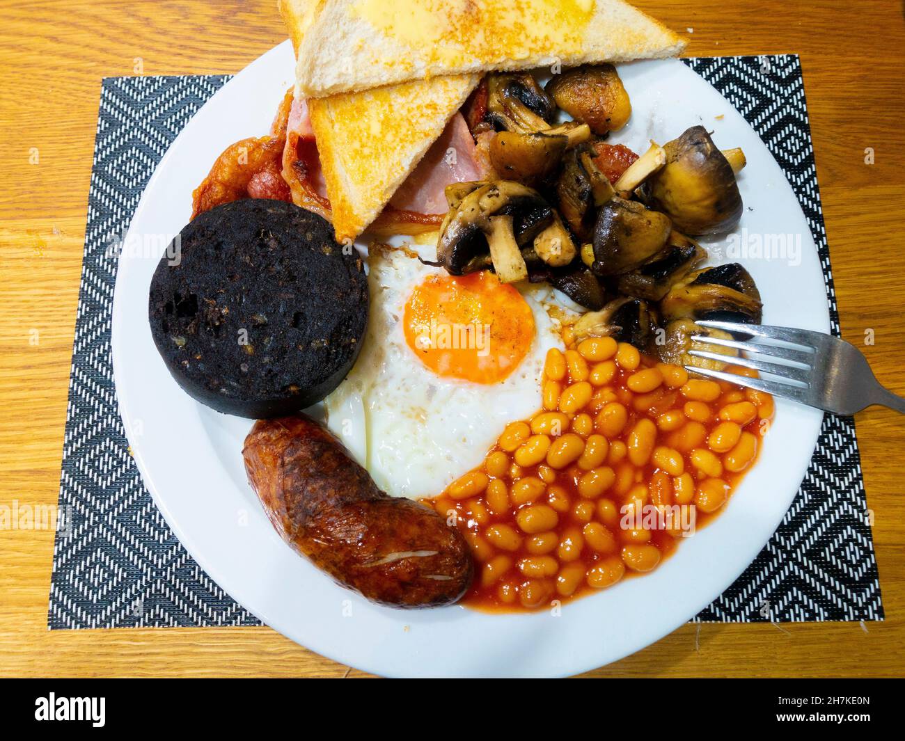 English farmhouse  Breakfast with well-done bacon fried egg sausages baked beans mushrooms and black pudding with white buttered toast Stock Photo