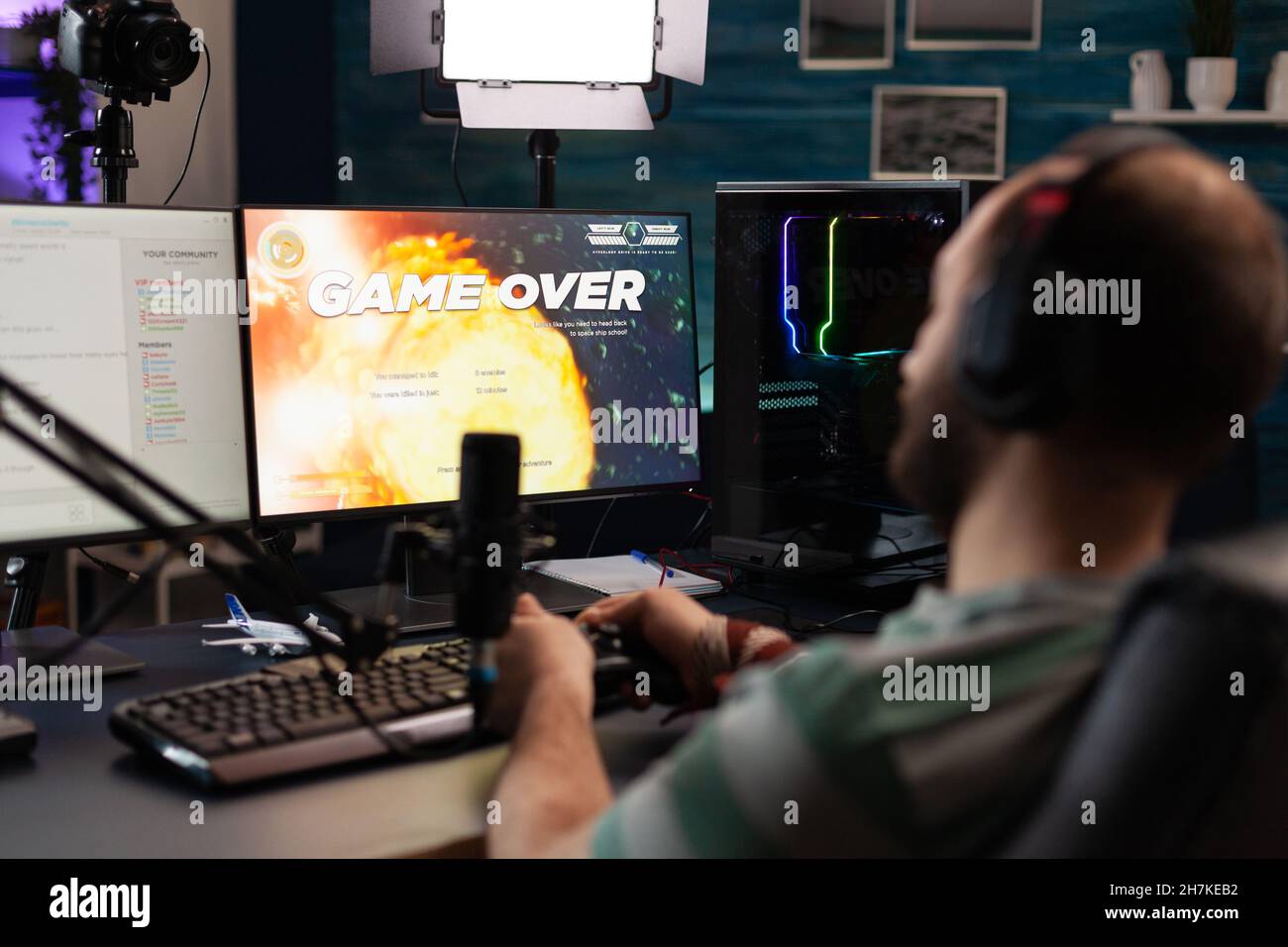 Man streaming video games with microphone and losing on computer. Gamer looking at monitors with live stream chat and online game, playing and broadcasting gameplay with headphones. Stock Photo