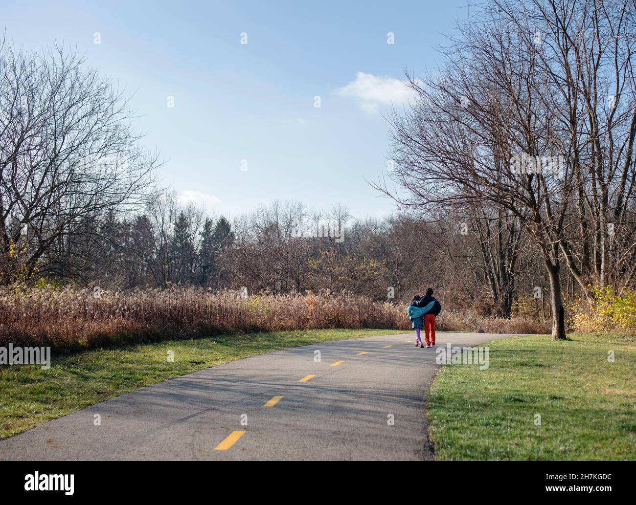 Two siblings walk arm-in-arm down path through park in autumn Stock Photo