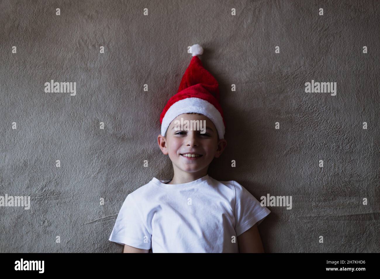 High angle view boy in a christmas hat smiling while lying on bed Stock Photo