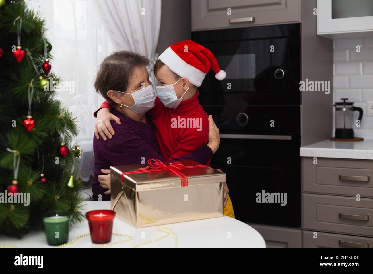 Young boy and grandmother in medical masks next to the christmas tree Stock Photo