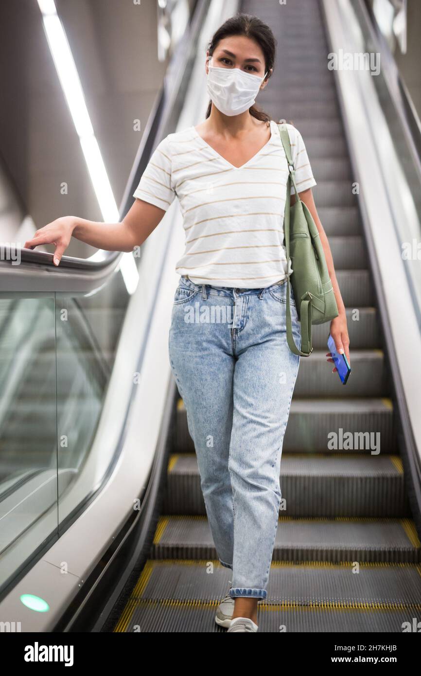 Woman in face mask going through escalator Stock Photo
