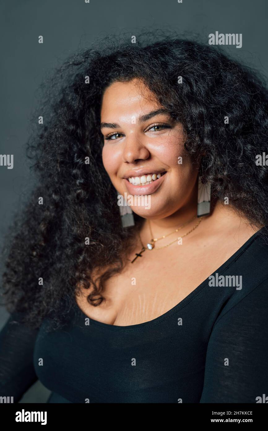 Voluptuous woman smiling against gray background Stock Photo Alamy