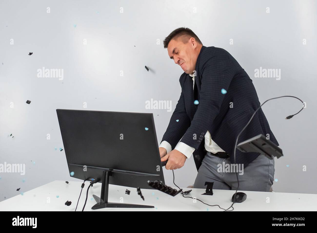 Caucasian man in a suit gets angry and smashes the keyboard on the monitor. An office worker in a rage breaks the computer. Stock Photo