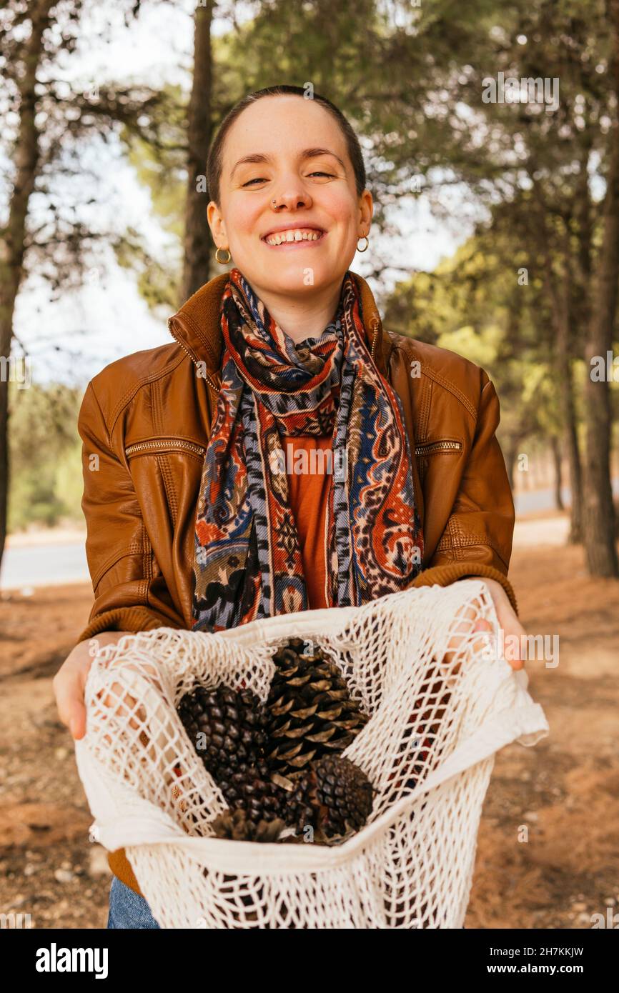 Smiling shaved head woman holding pine cones in bag Stock Photo