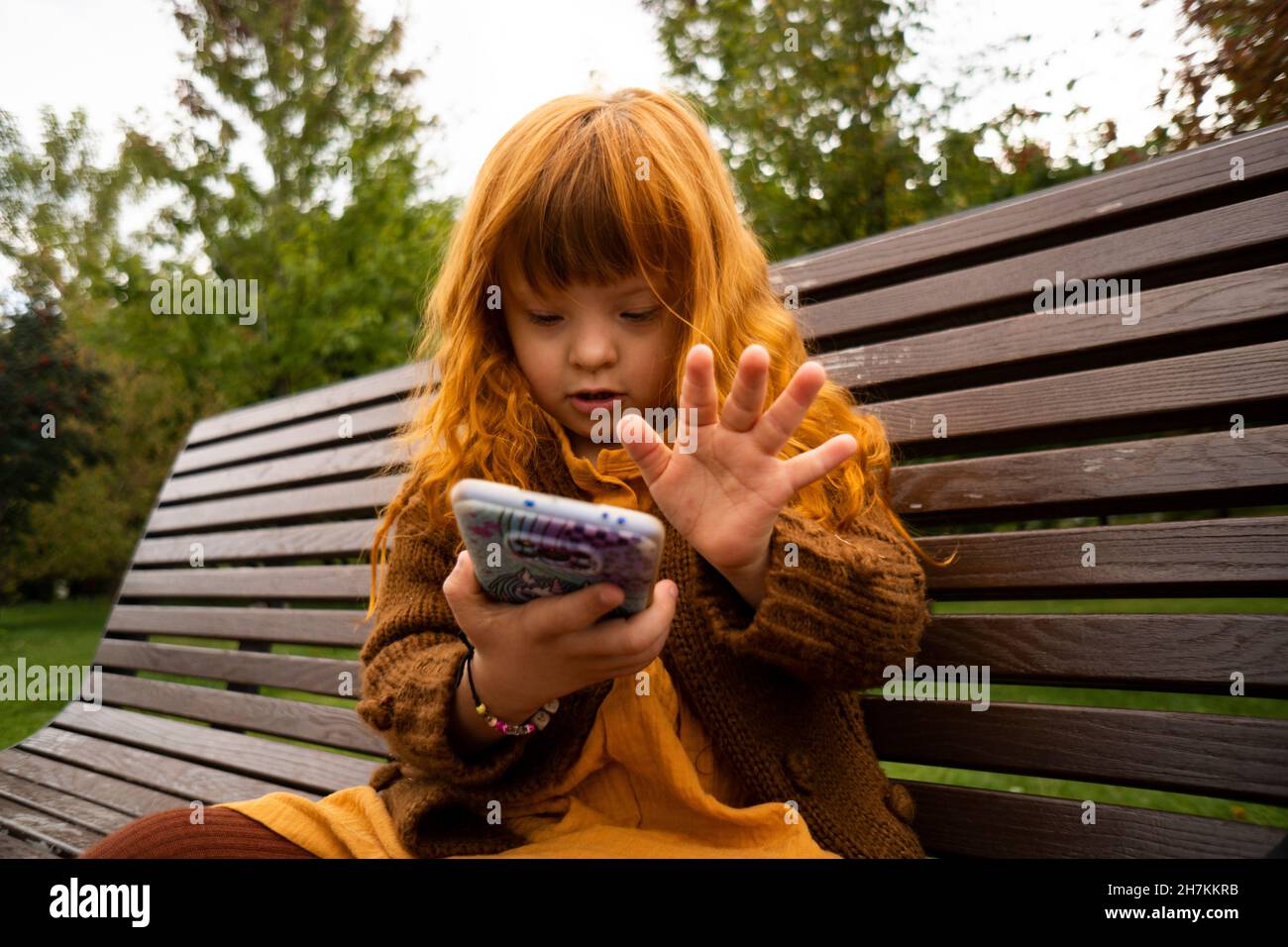 Redhead girl using mobile phone while sitting on park bench Stock Photo