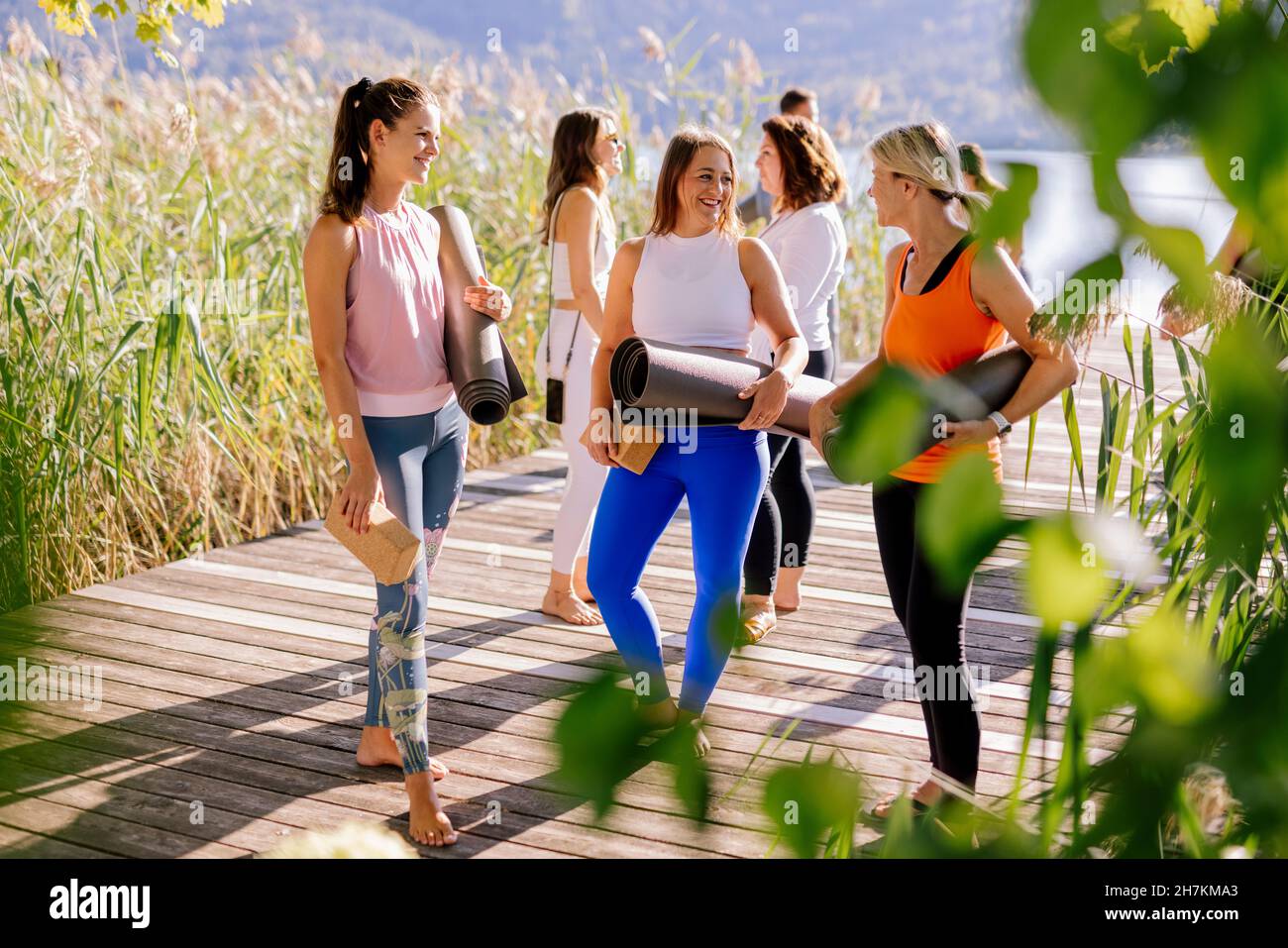 Women in sports clothing talking to each other while holding exercise mats Stock Photo