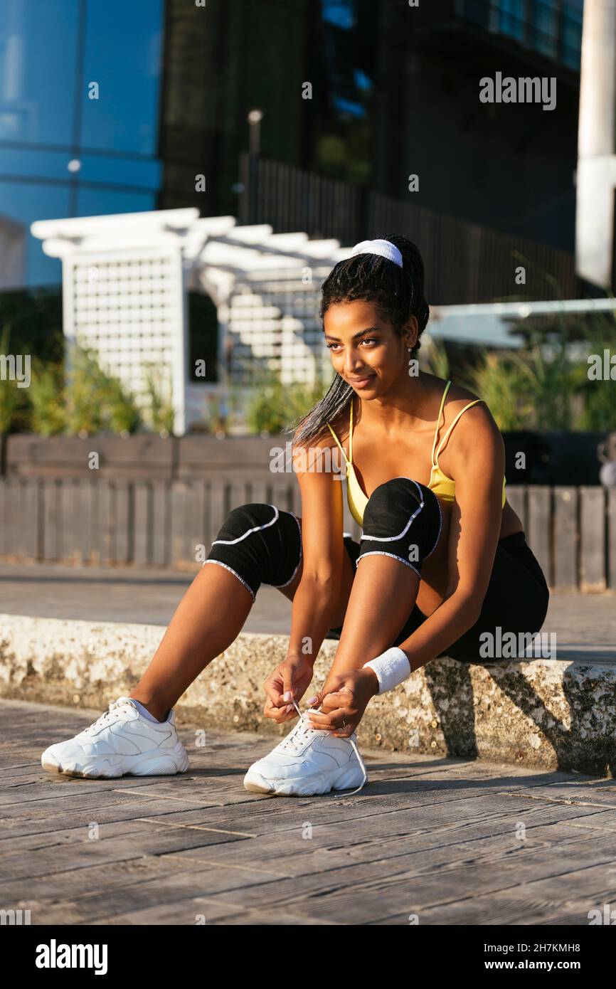 Smiling young athlete tying shoelace while sitting on curb Stock Photo