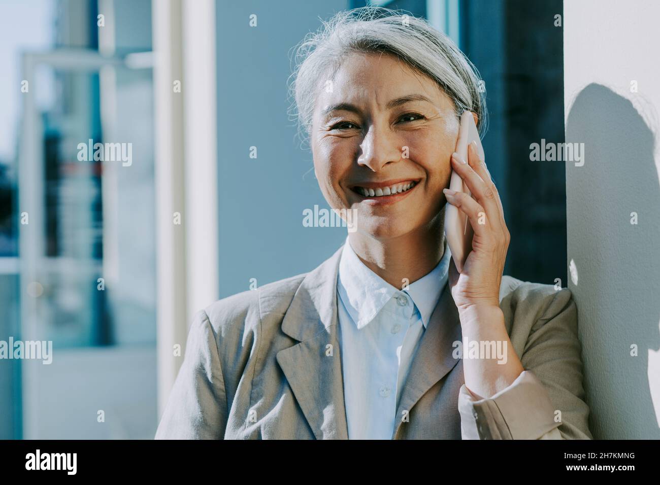 Happy mature woman talking on mobile phone by wall Stock Photo - Alamy