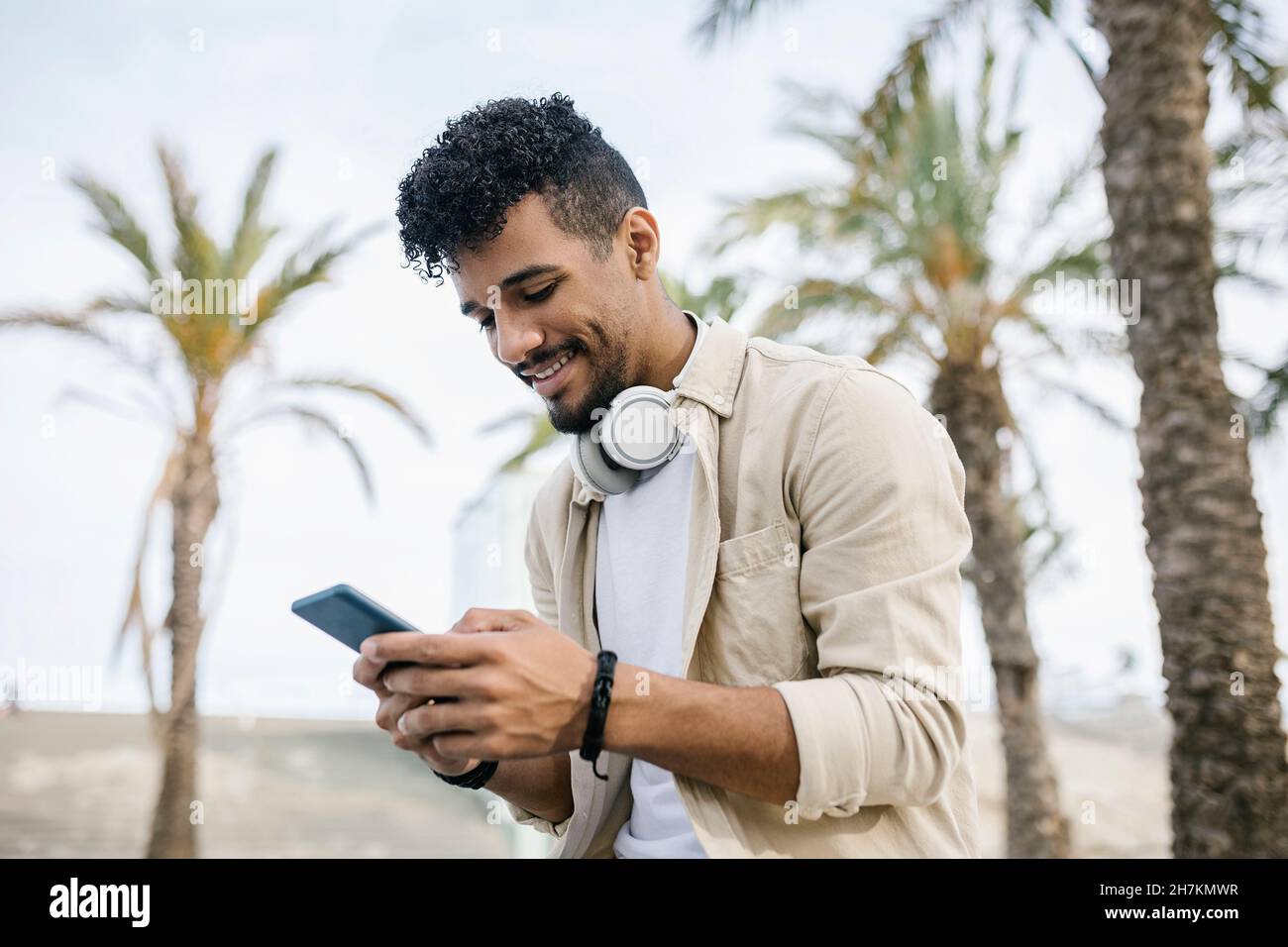Smiling man with wireless headphones text messaging through mobile phone Stock Photo